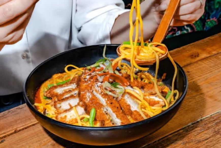 a close up shot of a katsu noodle bowl and someone taking a bite